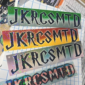 May include: Four rectangular stickers featuring the text JKRSMTD in a stylized black font. The stickers have holographic star patterns and different background gradients: green to white, orange to yellow, purple to white, and a pink, white, and blue stripe.