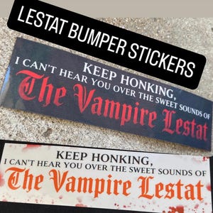 May include: Two rectangular bumper stickers featuring the text KEEP HONKING, I CAN'T HEAR YOU OVER THE SWEET SOUNDS OF The Vampire Lestat. One sticker has a black background with red lettering, while the other has a white background with red lettering.