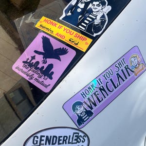 May include: A collection of stickers featuring gothic-inspired illustrations and text. The stickers include images of characters, a raven, and phrases like "Genderless Tenderness" and "Honk if you ship Wednesday and Enid."
