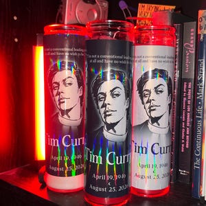 May include: Three cylindrical glass prayer candles featuring a black and white illustration of Tim Curry. Each label includes the text "I'm not a conventional leading man at all and have no wish to be" along with the name and birth and death dates.