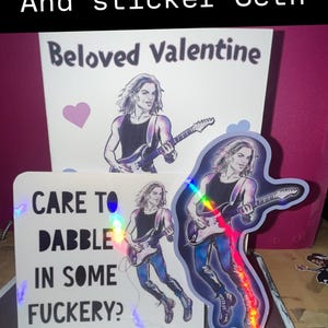 May include: Valentine's Day card and sticker set featuring a rockstar illustration. The card reads "Beloved Valentine" and "Care to dabble in some fuckery?" The set includes a sticker with a holographic effect.