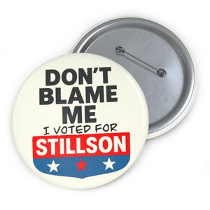 Könnte beinhalten: Ein runder Ansteckbutton mit cremefarbenem Hintergrund und dem schwarzen Text DON'T BLAME ME I VOTED FOR STILLSON. Unter dem Text befindet sich ein roter rechteckiger Balken und eine blaue Schildform mit drei Sternen, zwei weißen und einem roten.