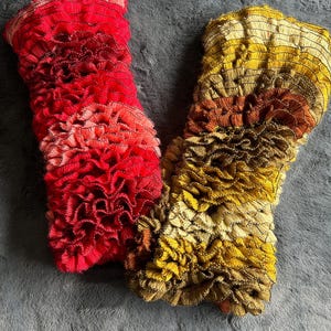 May include: Two fabric headbands with ruffled edges. One headband is red, pink, and orange. The other headband is brown, orange, and yellow.