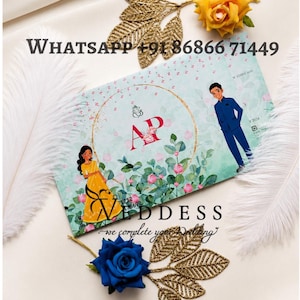 May include: A wedding invitation with a floral design, featuring illustrations of a couple. The invitation has the text "Goddess" and a phone number. Accompanying the invitation are gold leaf accents, a yellow rose, a blue rose, and white feathers.
