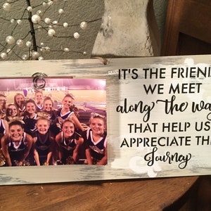 May include: A white wooden picture frame with a black and white photo of a cheerleading squad. The frame has a quote that reads "It's the friends we meet along the way that help us appreciate the journey."