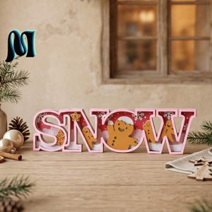 May include: A decorative wooden sign spelling the word SNOW in pink block letters. The interior of the letters features a layered scene with gingerbread figures, white snowflakes, and a red background, creating a festive holiday display.