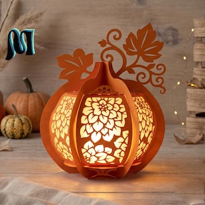 May include: A decorative orange pumpkin-shaped lantern featuring intricate laser-cut floral patterns on its panels. The structure includes a prominent stem and leaf design at the top, with a warm internal light illuminating the cutouts.