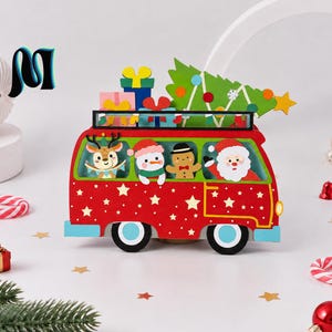 Op de afbeelding: Een rode houten kerstdecoratie in de vorm van een busje met een dakdrager vol kleurrijke cadeautjes en een groene kerstboom. Binnenin het busje staan figuren van een rendier, sneeuwpop, peperkoekmannetje en de Kerstman. Versierd met witte sterren.