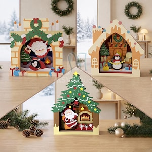 Può includere: Tre diorami natalizi decorativi in legno con ritagli a strati. Uno raffigura un camino con Babbo Natale e un pinguino, un altro una casa di pan di zenzero con un pinguino e il terzo un albero di Natale con Babbo Natale vicino al camino.