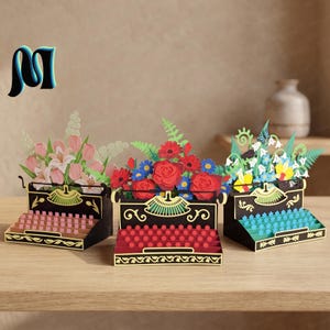 Op de afbeelding: Drie zwarte typemachine-sculpturen van papier met bloemstukken. De linker typemachine heeft roze tulpen, de middelste heeft rode rozen en blauwe bloemen, en de rechter heeft blauwe en gele bloemen met een kleine blauwe vlinder.