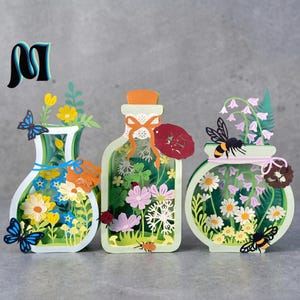 May include: Three-dimensional paper art featuring floral arrangements inside decorative bottles. The designs include butterflies, bees, and ladybugs. The color palette includes shades of green, white, yellow, and blue.