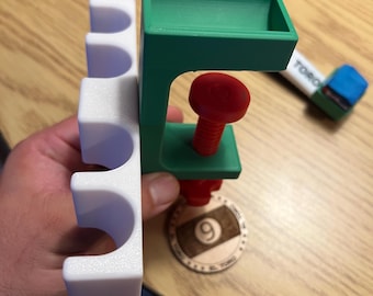 May include: A 3D-printed pool cue clamp in green, red, and white, holding a white pool cue holder. A wooden token with the number 9 is visible. The word "TORO" is printed on a blue and white object.