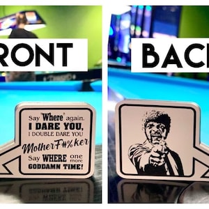 May include: A silver-colored, arrow-shaped metal sign with text from a movie quote on the front and a black and white image of a man pointing a gun on the back. The front says "Say Where again, I Dare You, I Double Dare You Mother F#%ker, Say WHERE one more GODDAMN TIME!"