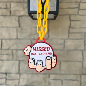 May include: A novelty sign with the text "MISSED BALL IN HAND" in red and white, shaped like a hand holding a ball. The sign is attached to a yellow chain, hanging from a black lantern.