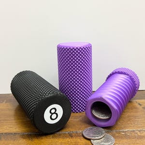 Könnte beinhalten: Drei Sparschweine, eines schwarz und zwei lila. Das schwarze Sparschwein hat eine weiße Zahl acht auf der Oberseite. Die lila Sparschweine haben ein strukturiertes Design. Ein lila Sparschwein ist offen und enthält Münzen.