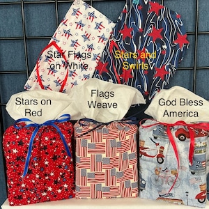 May include: Collection of fabric tissue box covers with patriotic themes. Designs include red, white, and blue stars, flags, and swirls. Each cover is a different pattern and has a coordinating ribbon tie.