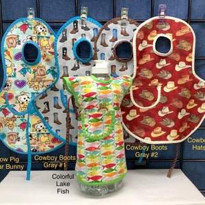 May include: Four different baby bibs with various designs. The bibs are made of fabric and have a pocket in the front. The designs include a cow and pig, cowboy boots, cowboy hats, and colorful fish. The text on the bibs reads "Cow Pig Bear Bunny", "Cowboy Boots Gray #1", "Cowboy Boots Gray #2", and "Cowboy Hats".