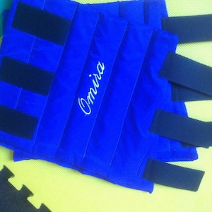 May include: Bright blue padded wraps with black straps and white stitching. The word "Omira" is embroidered in white script. The wraps are designed for a specific purpose, likely related to sports or therapy.