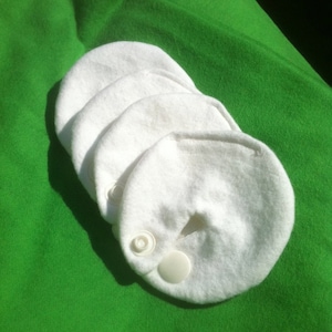 May include: Four white cotton burp cloths with a snap closure. The cloths are stacked on top of each other on a green surface.