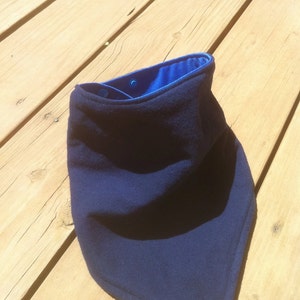 May include: A dark blue fleece neck warmer with a blue satin lining. The neck warmer is folded and lying on a wooden surface.