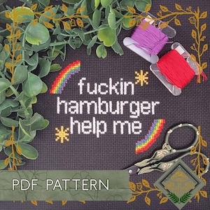 Peut inclure: Motif de point de croix avec le texte "fuckin hamburger help me" et des arcs-en-ciel et des étoiles. Comprend des bobines de fil rouge et violet, des ciseaux décoratifs et une bannière "PDF PATTERN".