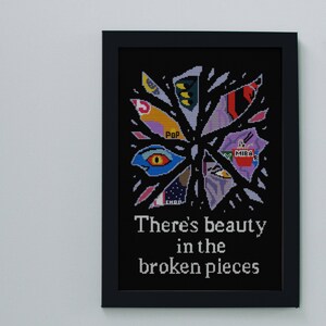 May include: Framed artwork with a black background featuring a colorful, abstract design of fragmented shapes. The artwork includes the text "There's beauty in the broken pieces" in white, with a black frame.