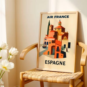 May include: A framed travel poster for Air France featuring a stylized illustration of a Spanish village with orange, yellow, and blue buildings. The poster is displayed on a wooden chair.