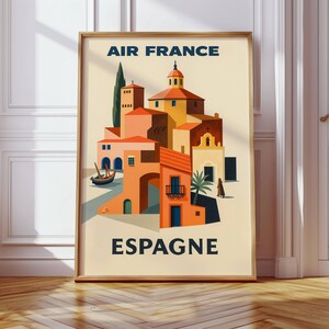 May include: A framed vintage travel poster for Air France featuring a stylized illustration of a Spanish village. The artwork showcases buildings in shades of orange, yellow, and brown, with the word "ESPAGNE" at the bottom.