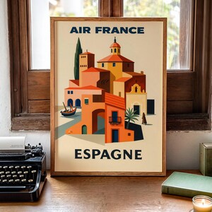 May include: A framed vintage travel poster for Air France, featuring a stylized illustration of a Spanish village. The artwork showcases buildings in shades of orange, yellow, and brown, with the word "ESPAGNE" at the bottom.