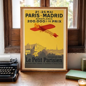 May include: Framed vintage travel poster for the Paris-Madrid air race, featuring a red biplane against a yellow background. The poster includes text in French, with the Eiffel Tower and other landmarks in the background.