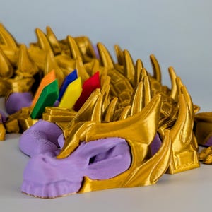 May include: A 3D printed dragon head with gold and purple paint. The dragon head has a spiky crown and a fierce expression.