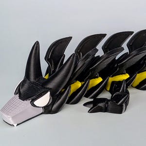 May include: A black and yellow segmented toy dragon with a gray head and white eyes. The dragon has a segmented body with black wings and yellow accents.