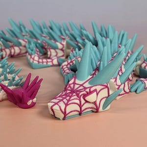 May include: A 3D-printed dragon sculpture with a white body, teal spikes, and a magenta web-like pattern on the head. The dragon's design features intricate details and a stylized aesthetic. The sculpture is a unique decorative item.