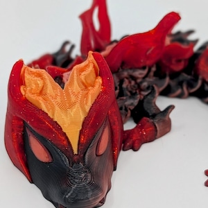 May include: A 3D-printed dragon figurine in shades of red, orange, and black. The dragon has a detailed, textured surface with flame-like features and a fierce expression. The figurine is set against a white background.