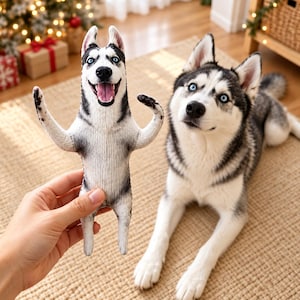 May include: A plush toy shaped like a Siberian Husky with black, white, and gray fur, blue eyes, and an open mouth. The toy features a printed design of the dog standing on its hind legs with arms raised, mirroring the appearance of a real Husky.