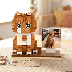 May include: A handmade Lego cat kit in shades of brown, tan, and white. The cat model has large eyes and a white bib. A small photo of a cat is displayed next to the model. The tag reads "Handmade Lego Cat Kit!"