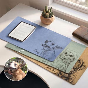 May include: A selection of desk mats with pet illustrations. Each mat displays a sketch of a dog or cat, with the pet's name beneath. A tablet is placed on the blue mat. A small cactus in a geometric pot is also visible.