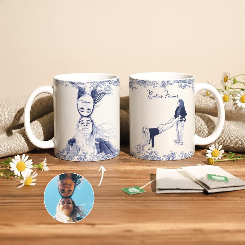 May include: Two white ceramic mugs with blue illustrations and floral patterns. One mug features two women's faces, the other shows two women in a playful pose with the text "Besties Forever".