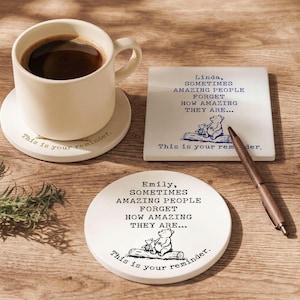 May include: A white ceramic mug filled with coffee sits on a matching coaster. Two additional coasters are visible, one square and one round, each with a Winnie the Pooh illustration and the text "This is your reminder."