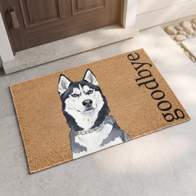 Puede incluir: Un felpudo rectangular de fibra de coco color canela con una ilustraci&oacute;n en blanco y negro de un Husky siberiano de ojos azules con un collar de cadena plateado. La palabra goodbye est&aacute; impresa en letras min&uacute;sculas negras a la derecha.