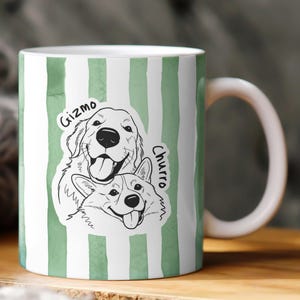 May include: White ceramic mug with a green watercolor stripe design. The mug features a black and white illustration of two dogs, a Golden Retriever and a Corgi, with the names "Gizmo" and "Churro" written above them.