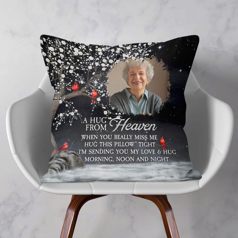 Peut inclure: Un coussin d&eacute;coratif avec une photo d'une femme, d'un arbre et d'oiseaux rouges. Le coussin porte l'inscription "A HUG FROM Heaven" et un message sur l'amour et les c&acirc;lins. Le coussin est sur une chaise blanche.