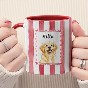 May include: A ceramic mug with a red handle and interior, featuring a vertical red and white striped pattern. The mug displays a watercolor illustration of a golden retriever dog with the name "Stella" in a decorative frame.