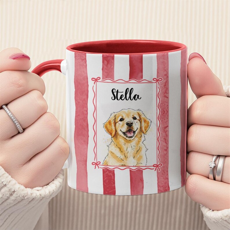 May include: A ceramic mug with a red handle and interior, featuring a vertical red and white striped pattern. The mug displays a watercolor illustration of a golden retriever dog with the name "Stella" in a decorative frame.