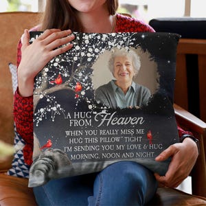 Peut inclure: Un coussin d&eacute;coratif avec une photo d'une femme &acirc;g&eacute;e, un arbre avec des cardinaux rouges et le texte "A Hug From Heaven". Le coussin a un fond sombre avec des accents blancs et un message touchant.
