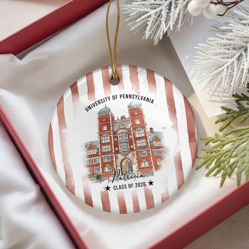 May include: A round ceramic ornament featuring a watercolor illustration of a university building. The ornament has a red and white striped background and includes the text "UNIVERSITY OF PENNSYLVANIA", the name "Patricia", and "CLASS OF 2026".