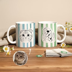 May include: Two white ceramic mugs with pet portraits. One mug has a blue and white striped pattern with a cat illustration and the name "Luccy". The other mug has a green and white striped pattern with dog illustrations and the names "Gizmo" and "Churro".
