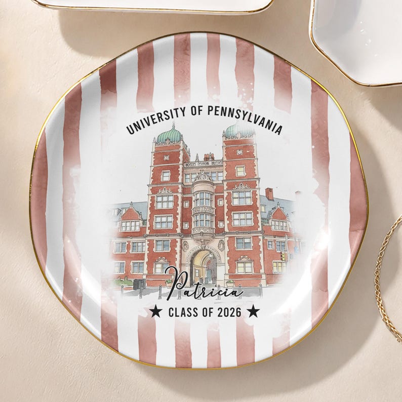 May include: A decorative plate with a gold rim and a watercolor design. The plate features a red and white striped pattern and a detailed illustration of a university building. Text includes "UNIVERSITY OF PENNSYLVANIA", a name, and "CLASS OF 2026".