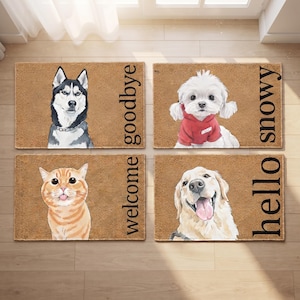 Puede incluir: Cuatro felpudos rectangulares de fibra de coco color canela con ilustraciones de animales y texto. Arriba a la izquierda: un husky con el texto goodbye. Arriba a la derecha: un perro blanco con sudadera roja y el texto snowy. Abajo a la izquierda: un gato naranja con el texto welcome. Abajo a la derecha: un golden retriever con el texto hello.