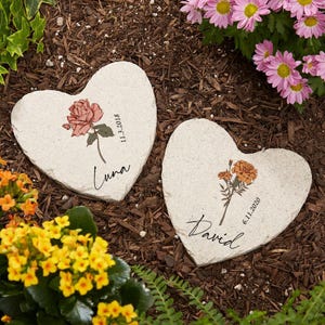Peut inclure: Deux galets de jardin en forme de cœur avec des motifs floraux et des noms et des dates personnalisés. Le galet de gauche a une rose rose et le texte "Luna 11.3.2018". Le galet de droite a un souci orange et le texte "David 6.11.2020".